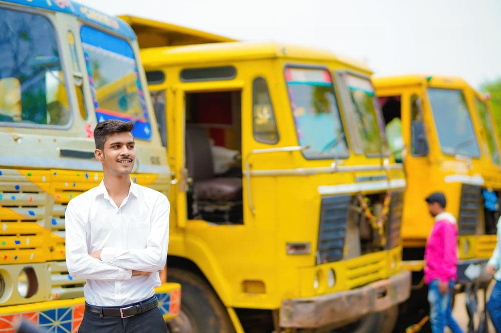 A smiling truck owner standing in front of his fleet of lorries