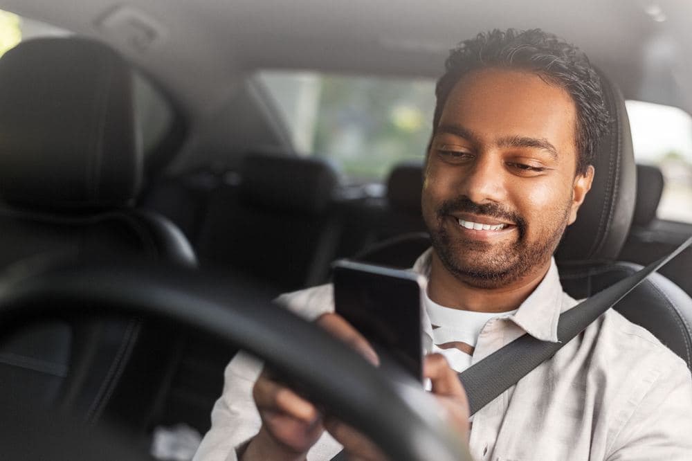 A smiling driver checking his phone in his car