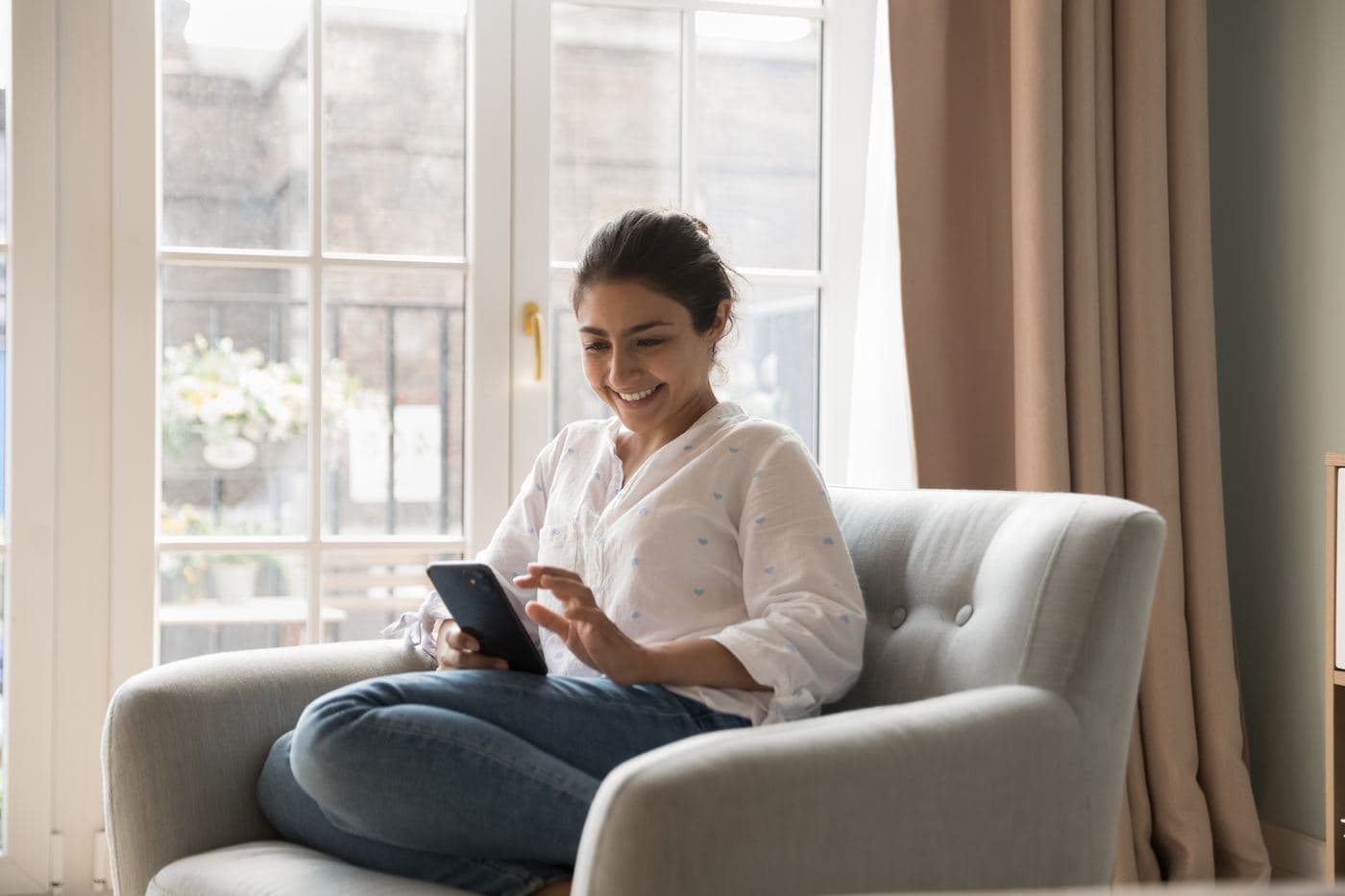 A woman relaxing in an armchair and smiling at her phone